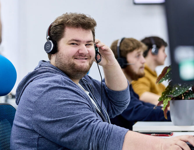 managed communications services with CYAN Solutions - Fully Managed Business IT Support. image: a helpdesk IT expert speaking with a customer on their headset, looking at the camera and smiling.